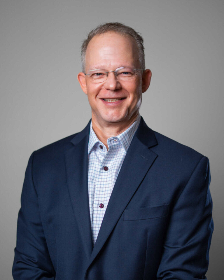 Smiling professional in a suit, representing Asset Enterprises' mission to enable and sustain critical retail technology.