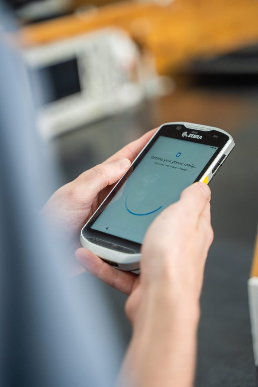 Person holding a Zebra device displaying "Getting your phone ready," highlighting payment visibility in retail environments.
