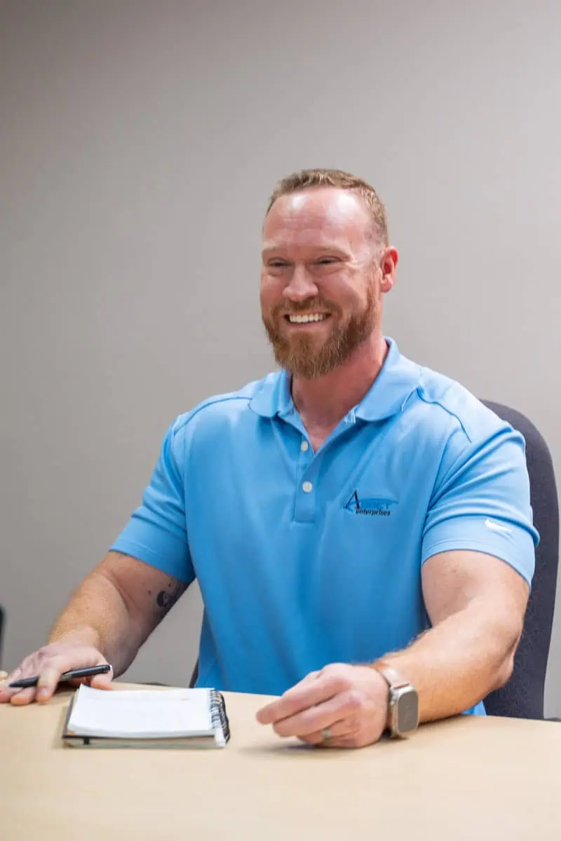 Smiling man in a blue polo sits at a desk with a notebook, representing product sourcing discussions.