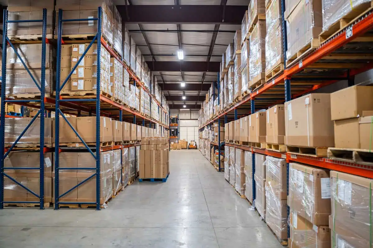 Warehouse aisle with stacked pallets and boxes, exemplifying where asset enterprises bring structured discipline.