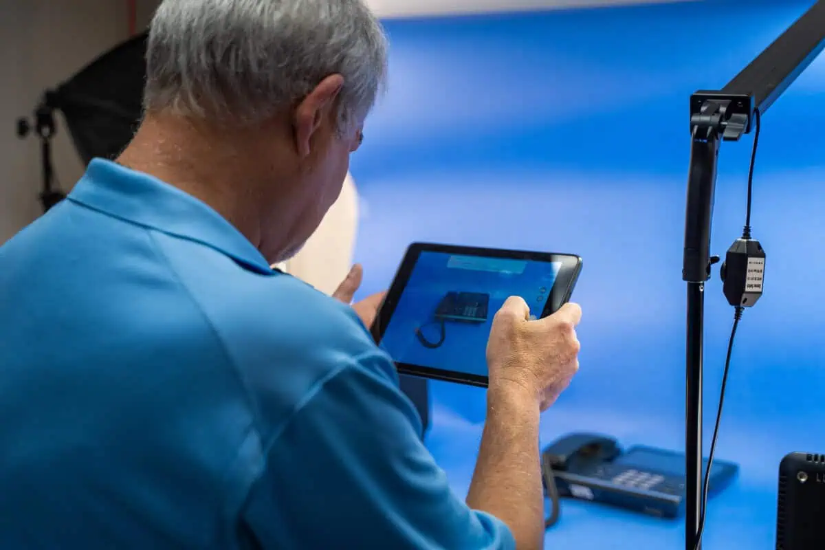Man in blue shirt using a tablet to photograph a product, highlighting product sourcing services.