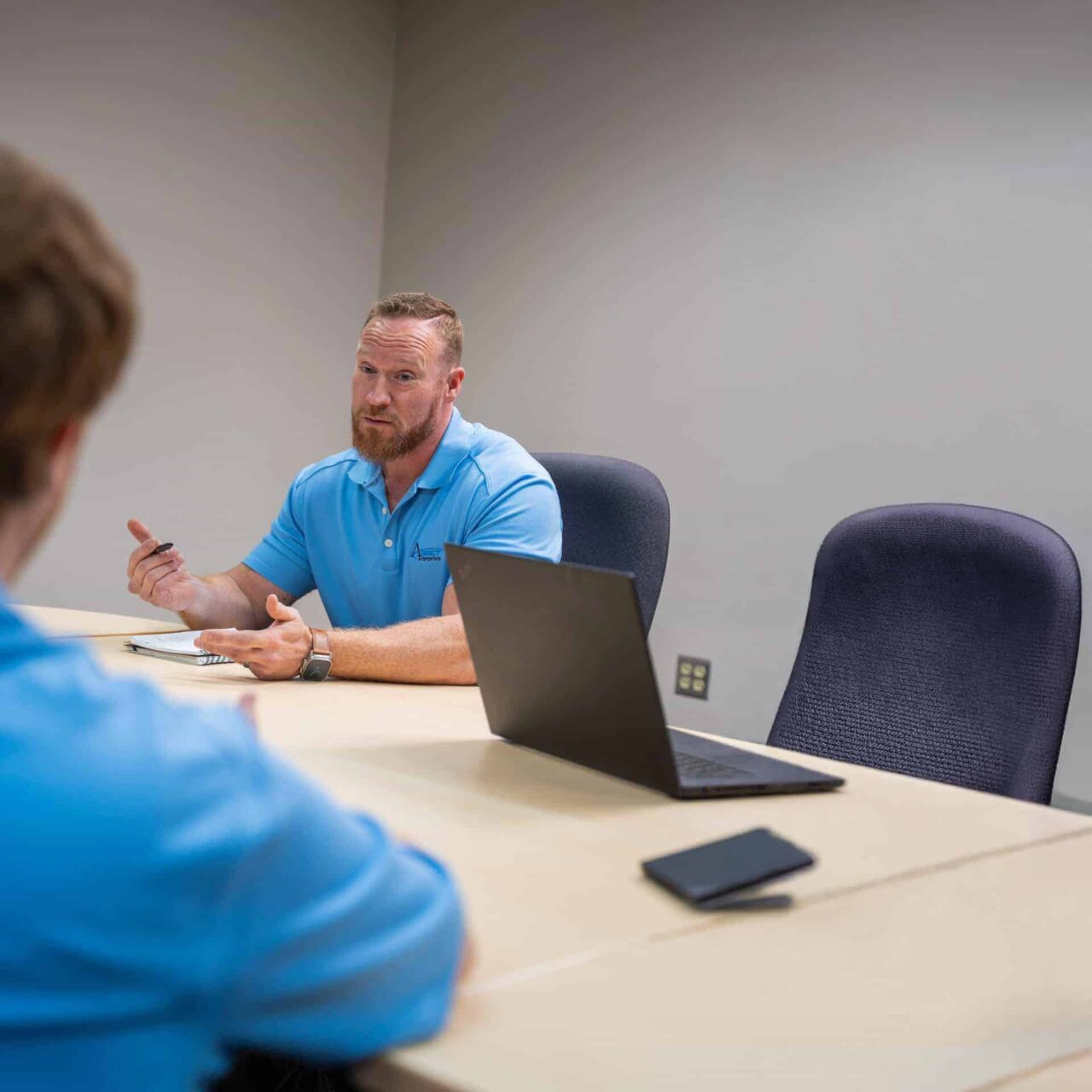 Man in blue shirt leading a meeting in office setting, discussing IT operations for Asset Enterprises.