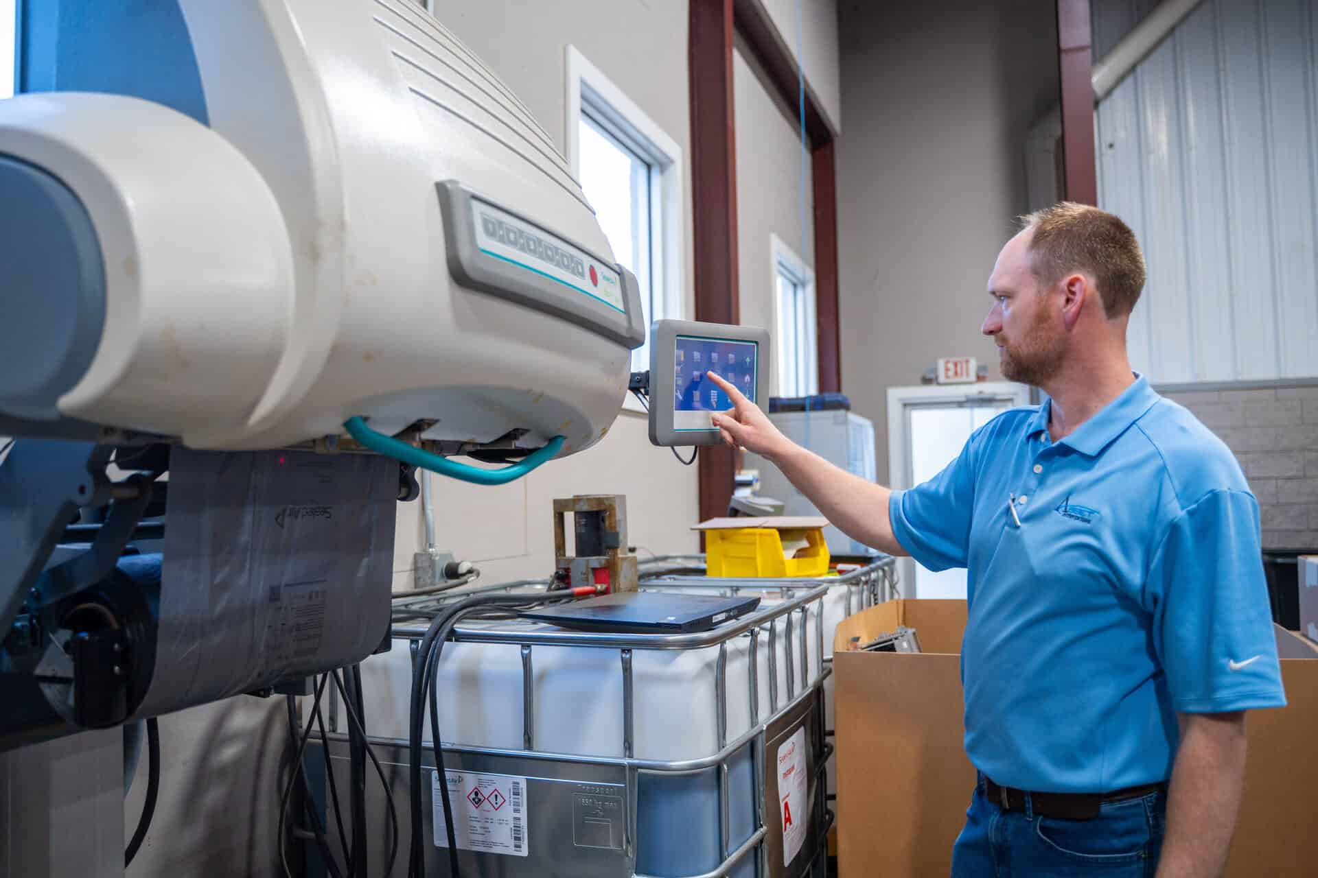 Technician in blue shirt operates equipment touchscreen at asset disposition facility, enhancing operations.