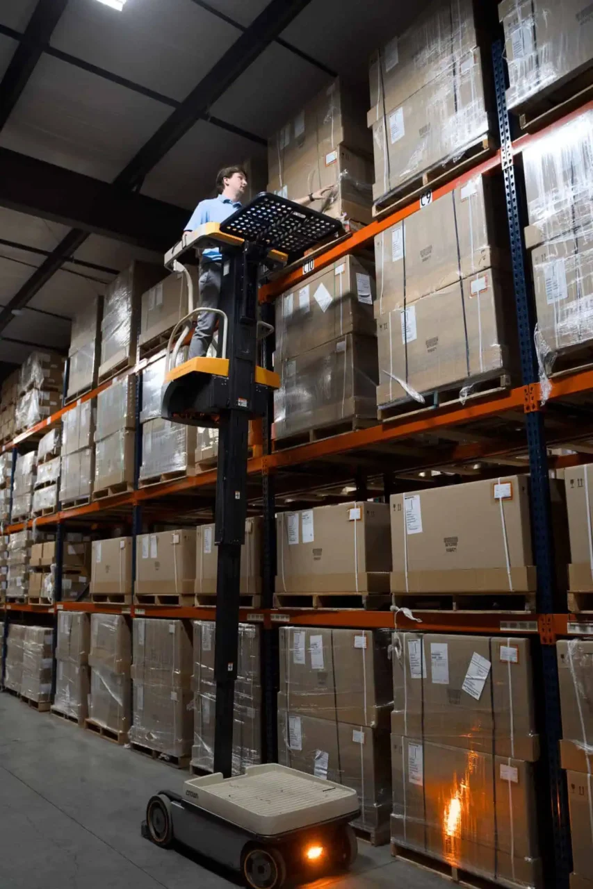 Warehouse worker on lift accessing high-shelved boxes, enhancing your operations at every location, every device.